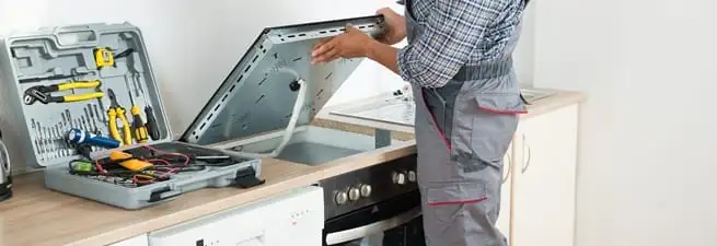 Cooktop repair technician lifting a built-in stovetop for service in Irvine, CA