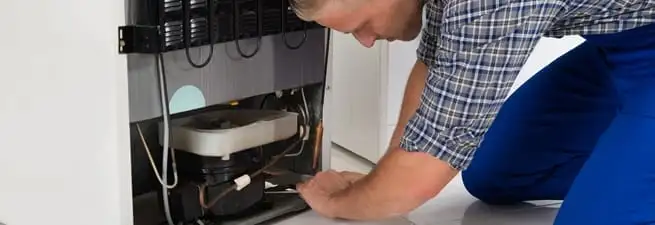 Refrigerator repair technician servicing the compressor and condenser area in Irvine, CA