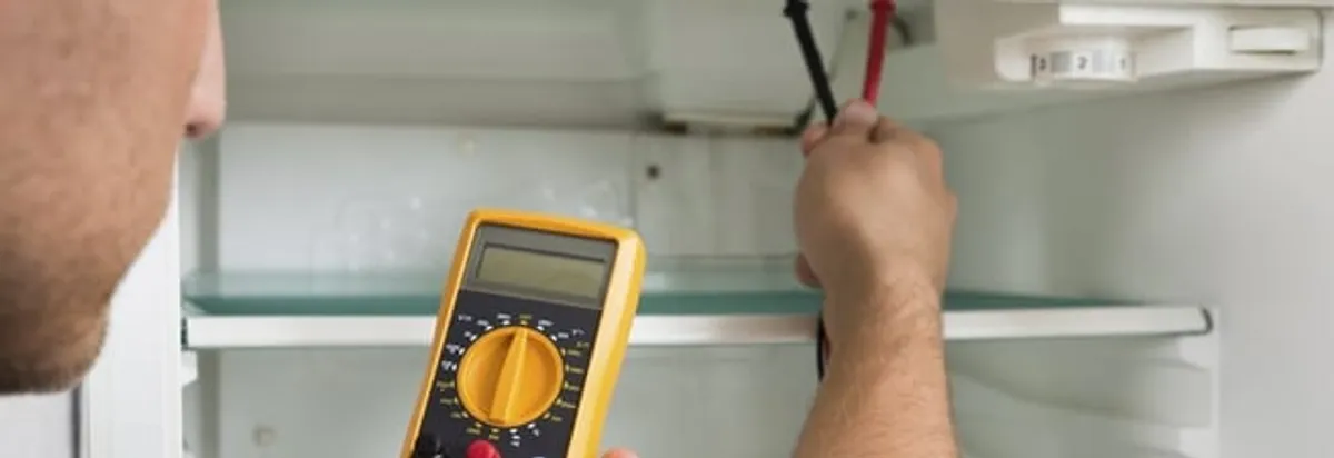 Refrigerator repair technician testing electrical components with a multimeter in Irvine, CA
