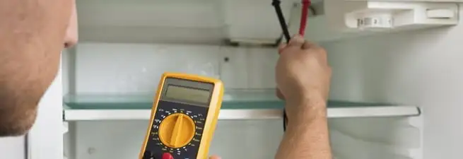 Refrigerator repair technician testing electrical components with a multimeter in Irvine, CA