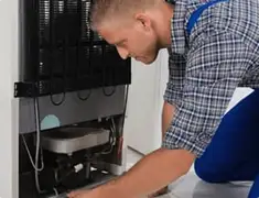 Refrigerator repair technician servicing the compressor and condenser area in Irvine, CA